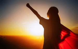 Oseba z dvignjeno roko ob sončnem zahodu kot simbol notranje moči, odgovornosti in zavestne manifestacije sprememb