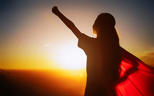 Oseba z dvignjeno roko ob sončnem zahodu kot simbol notranje moči, odgovornosti in zavestne manifestacije sprememb